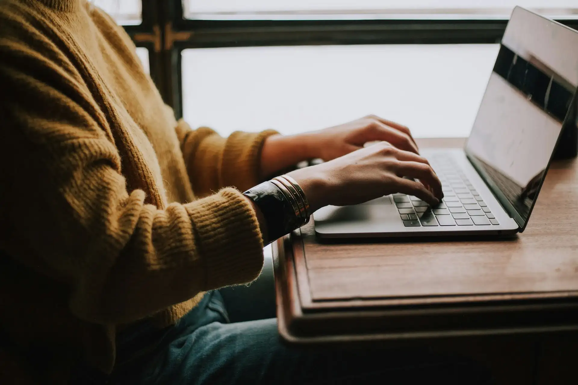 A person's hands typing on a computer keyboard, fingers moving swiftly across the keys. The person's posture suggests focus and engagement. The keyboard is clean and modern, with no discernible branding. The background is blurred, keeping the focus on the act of typing. The image conveys productivity and technology use.
