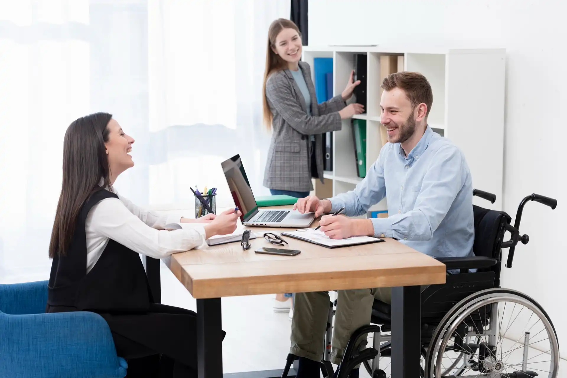 Disabled man meeting with two girls and working on a laptop with a pen an paper in his hand